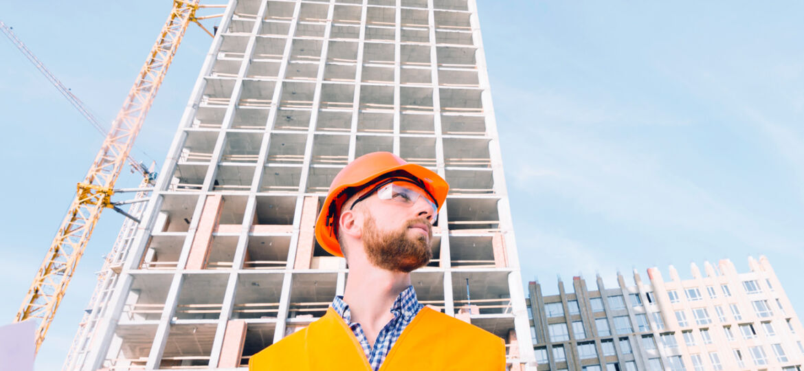 Construction worker in orange vest and helmet at building site.